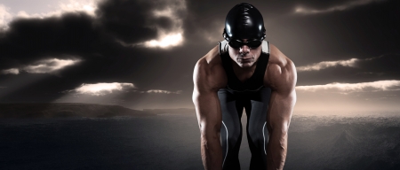 Swimmer triathlon man with cap and glasses outdoor at rough sea with stormy dark sky. Extreme fitness sport.の写真素材