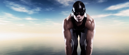 Swimmer triathlon muscled man with cap and glasses outdoor at a lake with blue cloudy sky. Extreme fitness sport.の写真素材