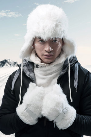 Asian winter fashion man in snow mountain landscape. Wearing black jacket with white furry hat and...