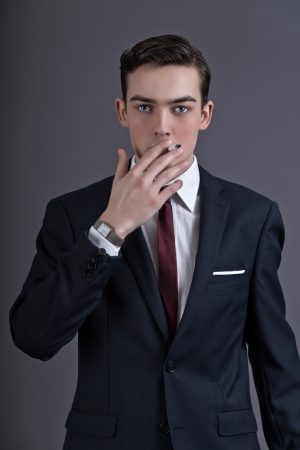 Retro fashion fifties young businessman wearing dark suit and tie. Smoking a cigarette. Studio shot against grey.の写真素材
