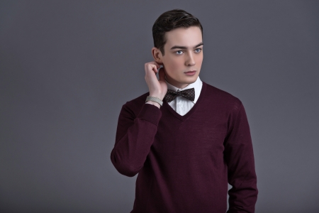 Retro fifties english style fashion young man. Wearing dark red shirt and bow tie. Studio shot against grey.の写真素材