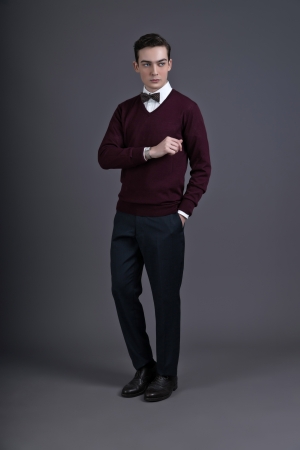 Retro fifties english style fashion man looking at his watch. Wearing dark red shirt and bow tie. Studio shot against grey.の写真素材