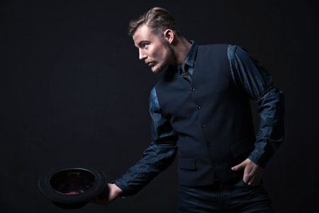 Retro 1900 modern fashion man. Wearing blue jeans shirt with gilet and trousers. Holding black hat....