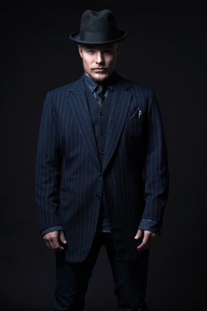 Retro 1900 modern fashion man with blonde hair and beard. Wearing blue striped suit and black hat. Studio shot against black.の写真素材