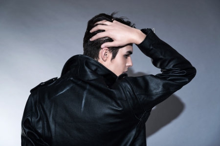 Cool retro rock and roll 50s fashion man. Hand in his hair. Wearing black leather jacket. Studio shot against grey.の写真素材