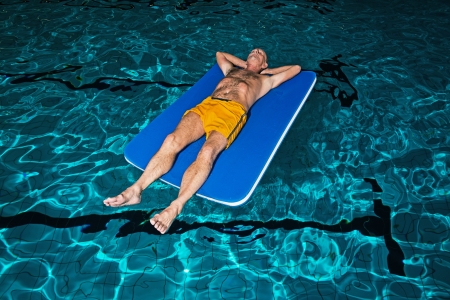 Healthy active senior man with beard in indoor swimming pool playing with foam raft.の写真素材