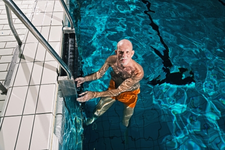Healthy active senior man with beard in indoor swimming pool. Wearing orange swimming trunks.の写真素材