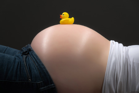 Pregnancy belly with yellow duck toy isolated on grey  Close-up の写真素材
