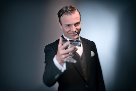Smiling retro 1920 business fashion man holding champagne glass. Raising his glass. Wearing black suit and bow tie. Studio shot.の写真素材