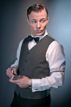 Retro classic business fashion man wearing grey gilet and bow tie. Holding silver cigarette case. Studio shot.の写真素材