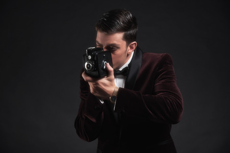 Well dressed business man taking picture with vintage camera. Wearing dark red dinner jacket with black bow tie.の写真素材
