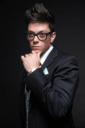 Stylish young business man wearing retro black glasses and dark blue striped jacket with tie. Studio shot against black.の写真素材