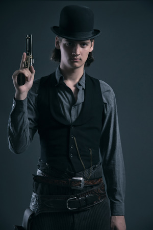 Western 1900 fashion man with brown hair and hat holding gun. Studio shot against grey.の写真素材