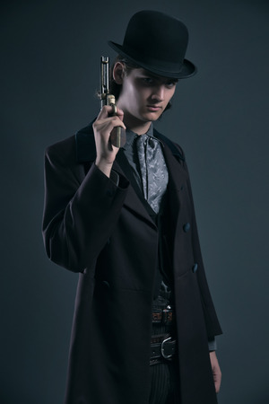 Western 1900 fashion man with brown hair and hat holding gun. Studio shot against grey.の写真素材