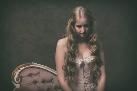 Vintage ballet fashion woman wearing pink corset and dress. Sitting on old sofa.の写真素材
