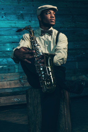 African american jazz musician with saxophone in front of old wooden wall.の写真素材