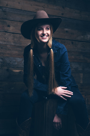 Cowgirl jeans fashion woman with long blonde hair. Sitting on wooden box in front of wooden wall.の写真素材