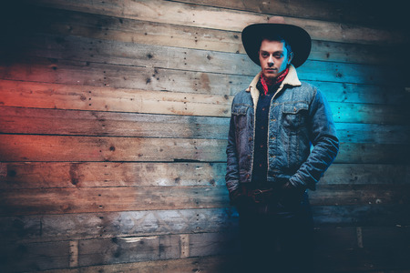 Winter cowboy jeans fashion man. Wearing brown hat, jeans jacket and trousers. Leaning against old wooden wall.の写真素材