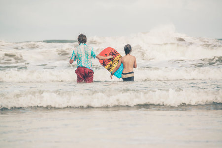 Father and son walking with bodyboard into the waves of ocean.