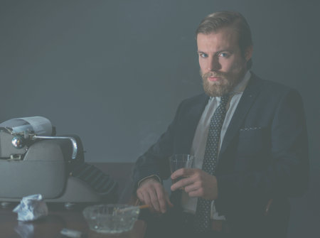 Moody portrait of a stylish vintage businessman sitting relaxing at his desk in the office in front...
