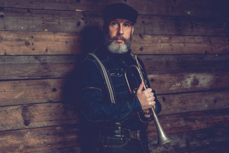 Half Body Shot of an Adult Male Musician Wearing Black Clothing with Ivy Cap Holding a Trumpet...