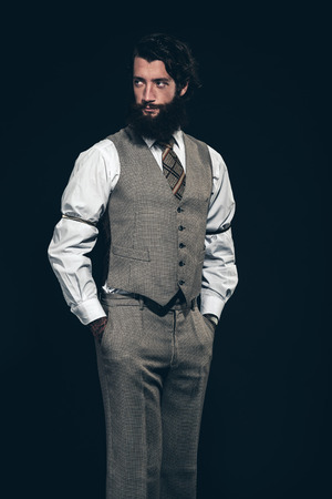 Relaxed attractive bearded businessman standing with his hands in his pockets looking back over his shoulder with a serious expressionの写真素材