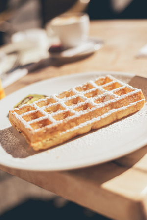 Close Up of Breakfast or Dessert Waffle on Plate Dusted with Icing Sugar on Outdoor Table in Sunの写真素材