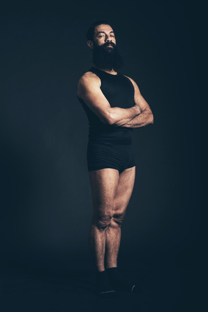 Portrait of a Confident Athletic Man, with Long Goatee Beard, Standing Straight with Arms Crossed and Looking at the Camera on a Black Background.の写真素材
