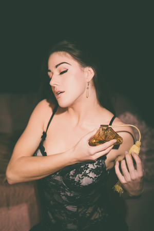 Close up Seductive Young Woman in Black Lace Nightwear Putting Perfume on her Body with Eyes Closed.の写真素材