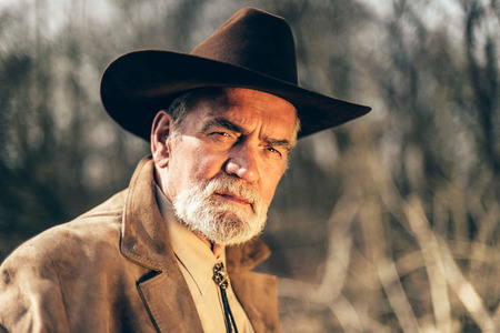 Handsome senior man with a speculative expression wearing a wide brimmed Western hat staring intently at the cameraの写真素材