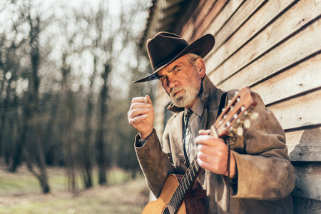 Close up Serious Western Male Guitarist Staring at the Camera While Leaning on the Wooden Wall of a House.の写真素材