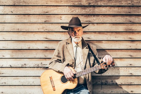 Portrait of a Serious Middle Age Male Guitarist Leaning on Wooden House Wall with Horizontal Pattern and Looking at the Camera.の写真素材