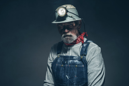 Close up Middle Age Male Mine Worker with Turned on Light on his Helmet, Looking at the Camera Seriously Against Gray Gradient Background.の写真素材