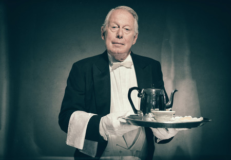 Waist Up Portrait of Professional Looking Senior Male Butler Wearing Tuxedo and Holding Tray with Tea Service for One with Pot and Cupの写真素材