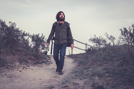 Backpacker walking down a sandy trail away from a viewpoint on a hilltop, low angle view approaching the cameraの写真素材