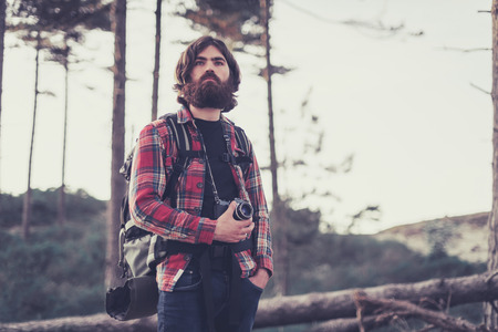 Photographer out on a camping trip standing with his camera around his neck wearing a large backpack staring into the distance, sandy trail with copyspaceの写真素材