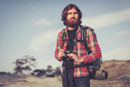 Handsome male backpacker with a camera in the wilderness following his hobby and passion for...