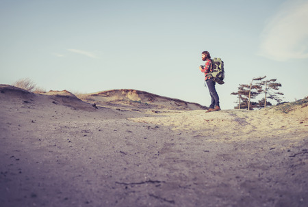 Nature photographer out on the trail standing in sandy terrain taking a photo in the distance with a backpack on his backの写真素材