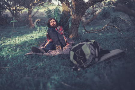 Backpacker relaxing in the shade of a tree reclining on a mat as he takes a break during the midday heatの写真素材