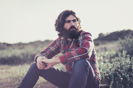 Backpacker taking a rest in the wilderness sitting on the ground relaxing and staring thoughtfully into the distanceの写真素材
