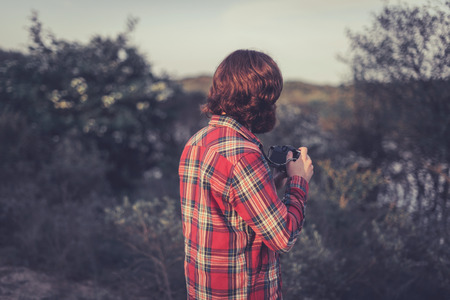 Wildlife photographer out in the wilderness standing with his back to the camera watching an area of trees and scrubの写真素材