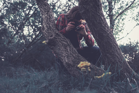 Photographer taking a photo of a fungus growing on a tree in the wilderness kneeling down for a better angle and focusの写真素材