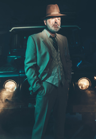 Serious Senior Bearded Businessman Standing While Smoking In Front of his Vintage Four-Wheel Vehicle at Night.の写真素材