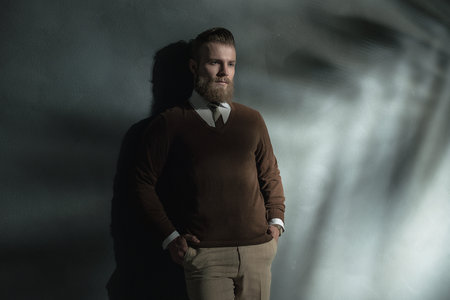 Handsome relaxed man with a thoughtful expression standing against a wall staring down at the ground...