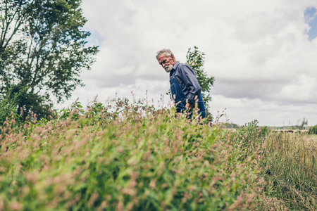 Middle Aged Bearded Male Farmer Looking at the Small Plants Growing on the Farm in the Morning.