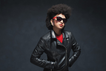 Half Body Shot of a Stylish Young Woman Wearing Black Leather Jacket with Sunglasses Against Black Background.の写真素材
