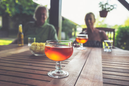 Alcoholic Cocktail Drink on Wooden Garden with Blurred Couple in Background.