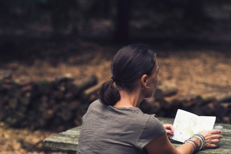 Rear View of Brunette Woman Reading Map at Wooden Table in Forest.の写真素材