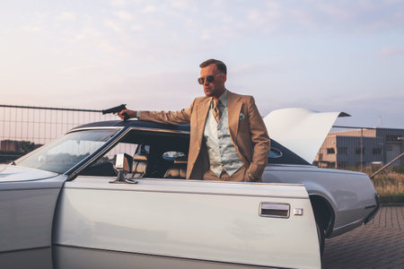 Retro 1970s gangster with pistol leaning against vintage car.