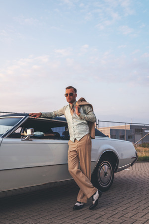 Retro 1970s fashion man leaning with arm on roof of vintage car.の写真素材